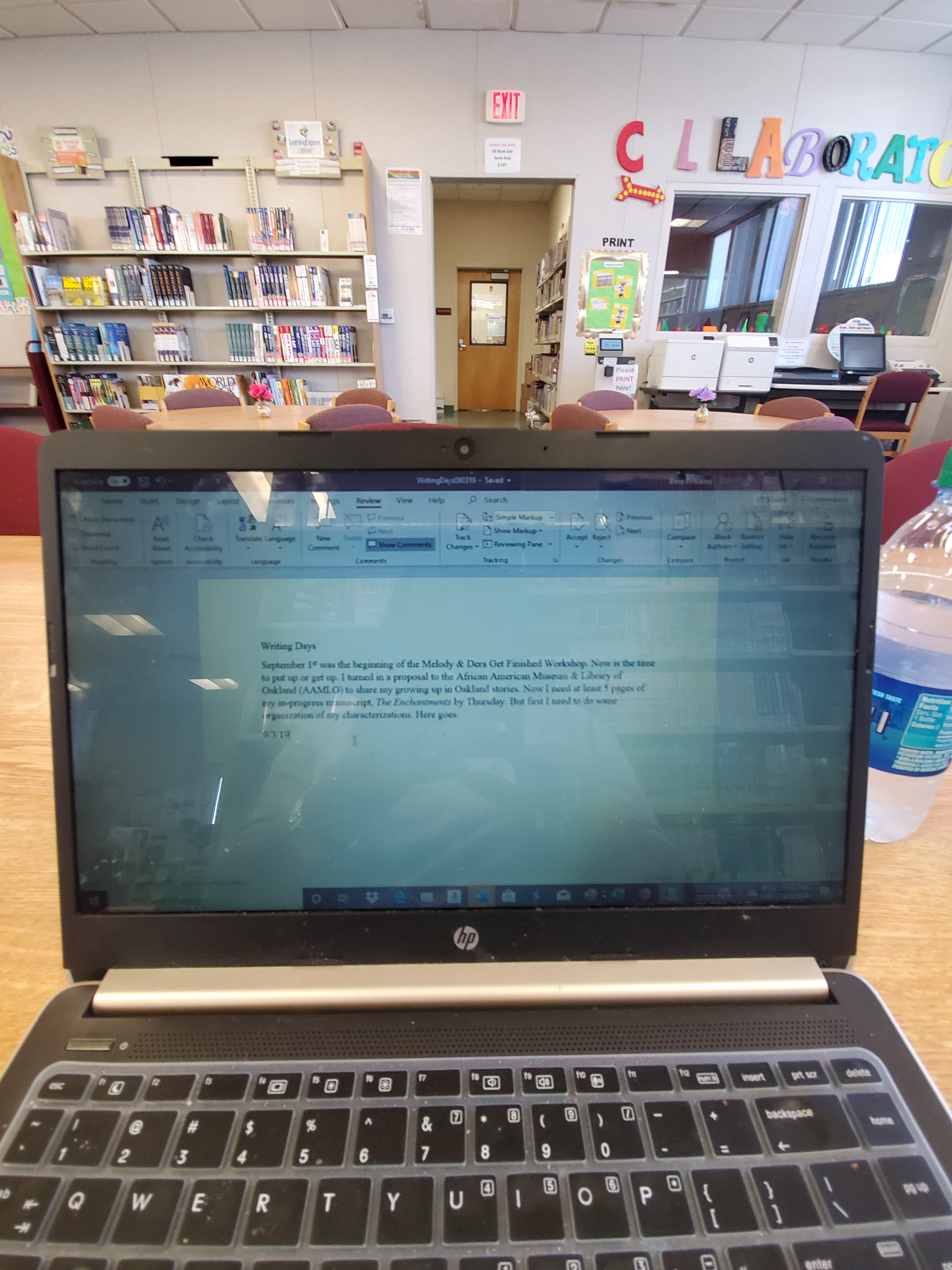 authors black laptop computer on wooden tabletop in a school library with short story on screen